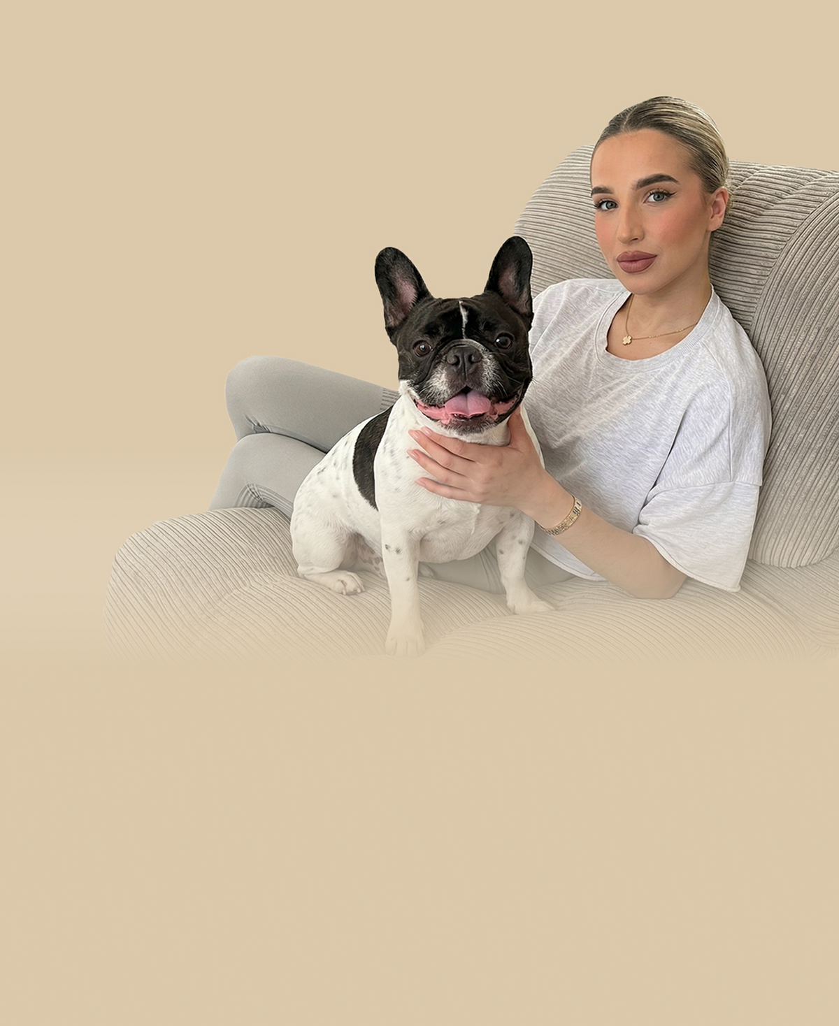 Woman sitting on a couch with a small black and white french bull dog, both looking at the camera against a beige background.