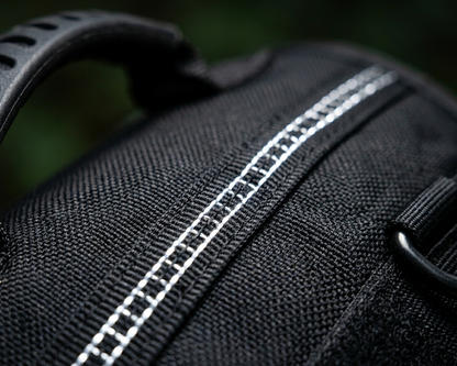 Close-up of a black dog harness with white stitching on a dark background